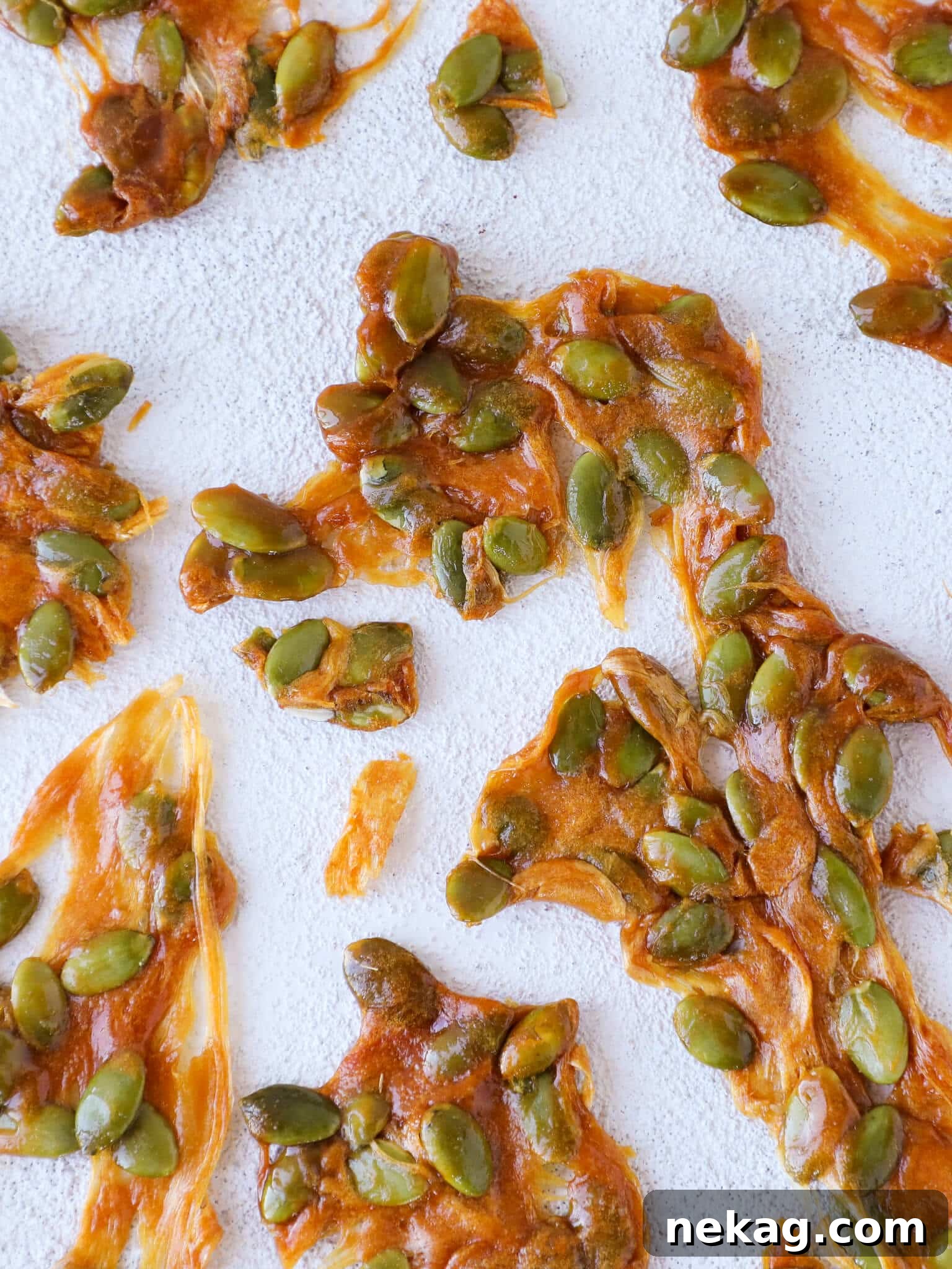 Caramel pumpkin seed brittle pieces on a clean white background, ready to be enjoyed.