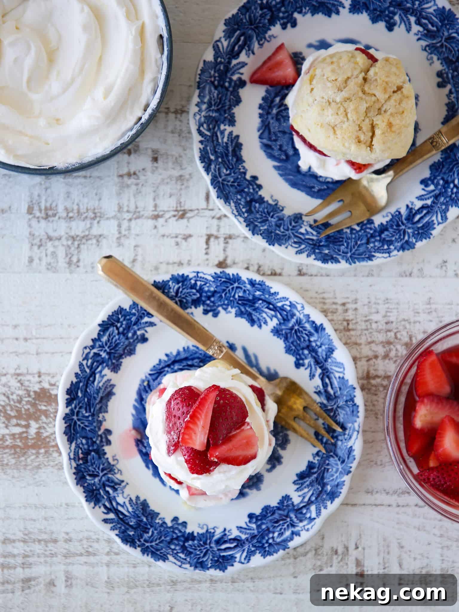 Strawberry Shortcake for Two blue china plates. A beautifully plated individual strawberry shortcake, topped with generous dollops of lemon whipped cream and glistening macerated strawberries, set against elegant blue china.