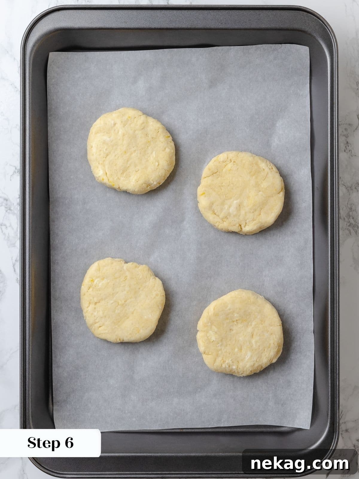 Biscuit dough rounds on a baking sheet after chilling. Chilled biscuit dough rounds, brushed with cream and sprinkled with sugar, arranged on a parchment-lined baking sheet, ready for the oven.