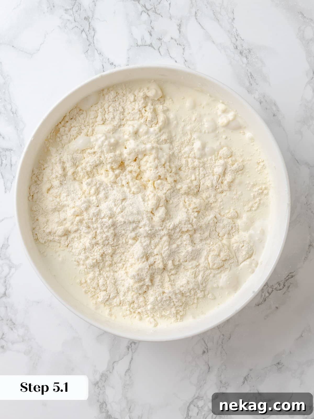 Starting to bring the shortcake dough together with cream. A mixing bowl with shortcake dough beginning to form, with liquid being incorporated to bring the dry ingredients together.