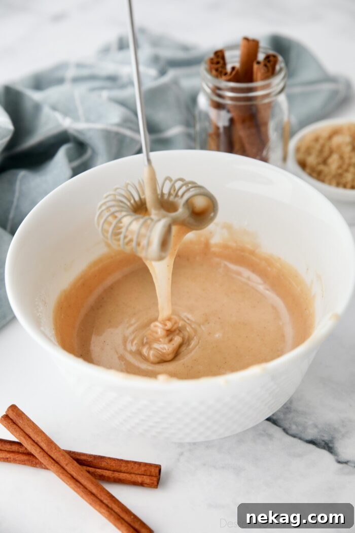 Golden Cinnamon Drizzle 2 Cinnamon brown sugar glaze dripping off of a whisk into a bowl.