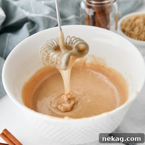 Cinnamon brown sugar glaze dripping off of a whisk into a bowl.