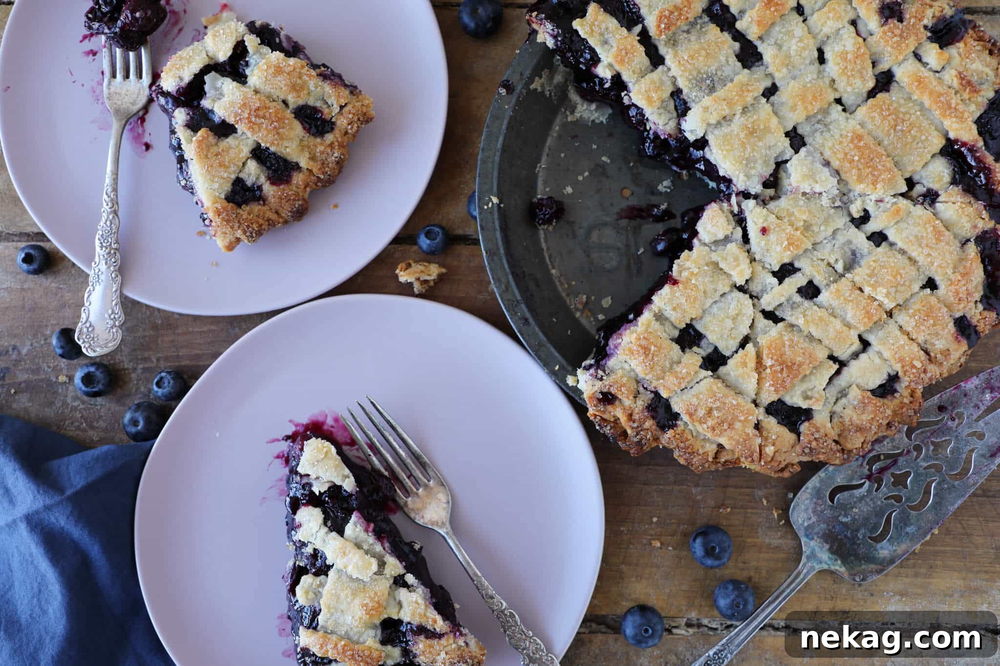 Two generous servings of blueberry pie artfully arranged next to a whole, golden-crusted blueberry pie on a rustic wood surface.