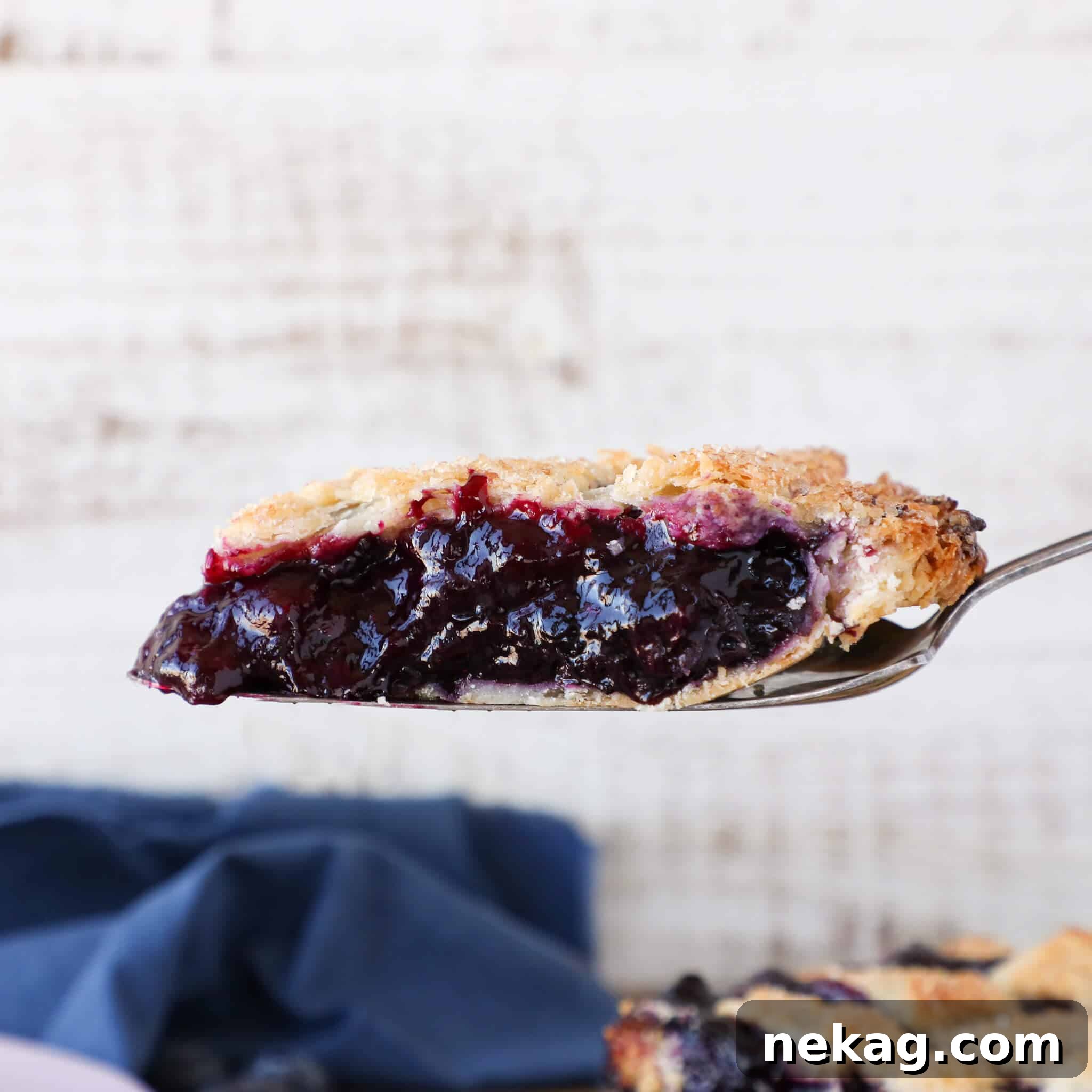 A slice of blueberry pie elegantly lifted on a pie server, showcasing its remarkably thick and perfectly set filling.