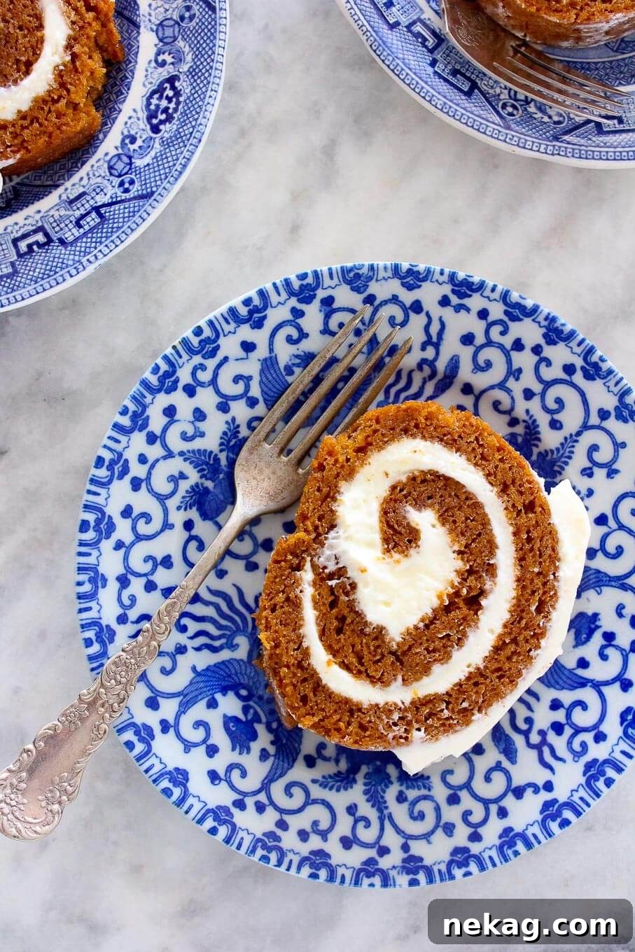 A slice of Pumpkin Roll with a vintage fork, revealing layers of cake and cream cheese filling.