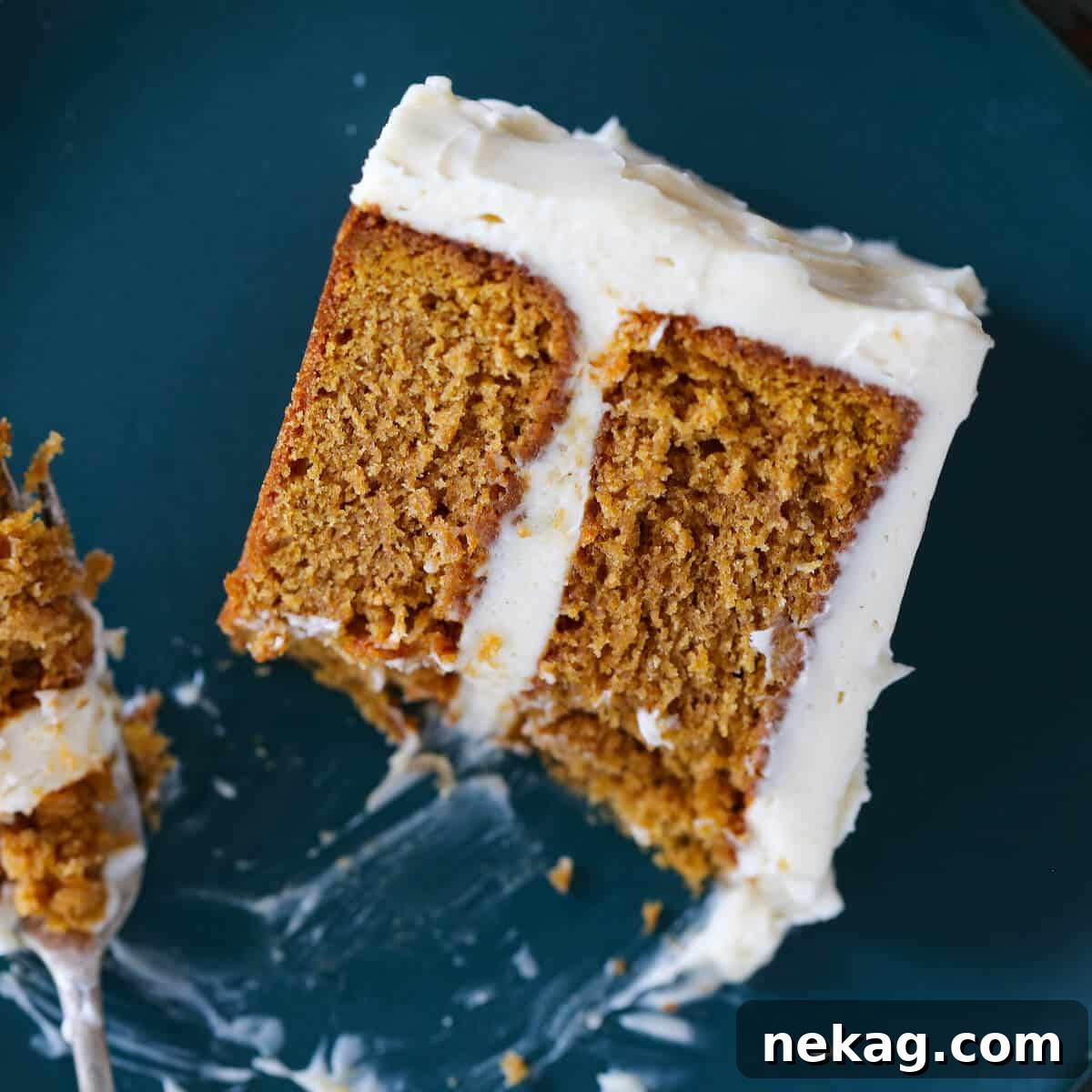 A slice of Pumpkin Spice Layer Cake with a bite taken, showing its fluffy texture and frosting layers.