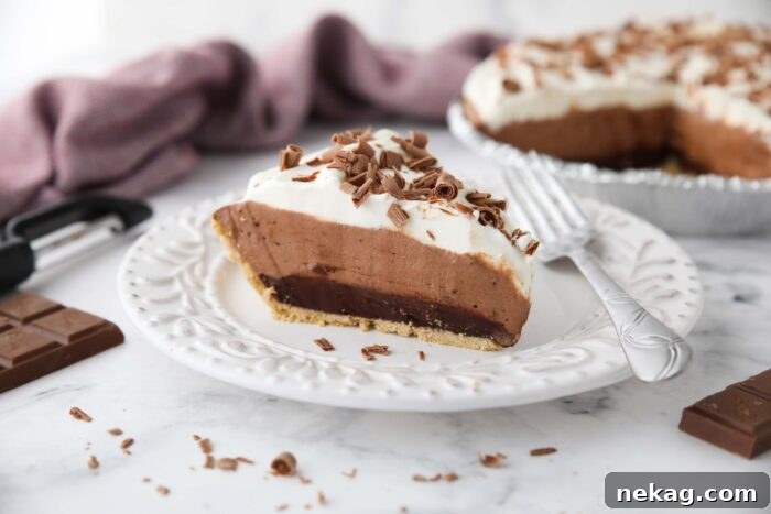 Decadent Chocolate Dream Pie 12 Slice of chocolate truffle pie on a plate showing a graham cracker crust and layers of ganache, whipped chocolate, whipped cream, and chocolate shavings on top.