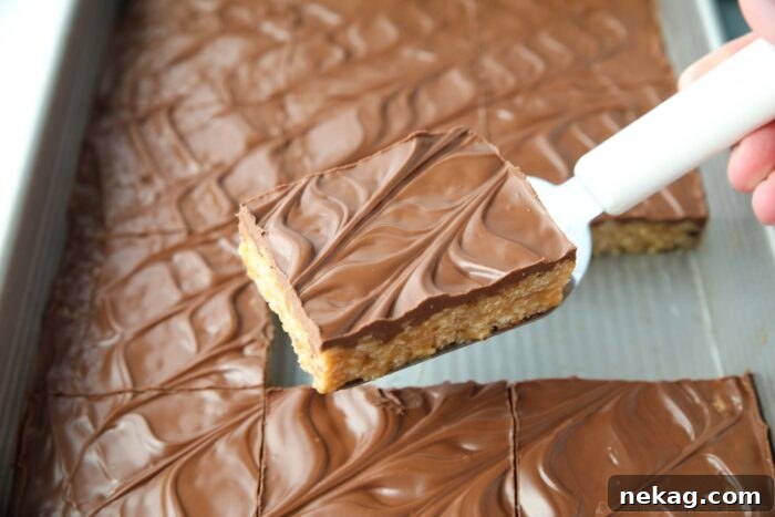 A scoop lifting a single perfect Scotcharoo bar from the pan, highlighting its layered texture and glossy topping.