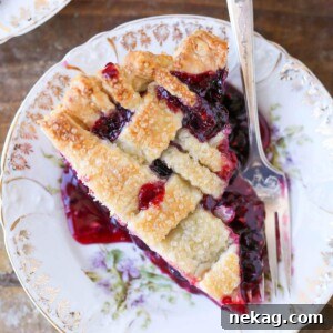 A serving of mixed berry pie with a golden lattice top and a silver fork, highlighting a perfect slice.