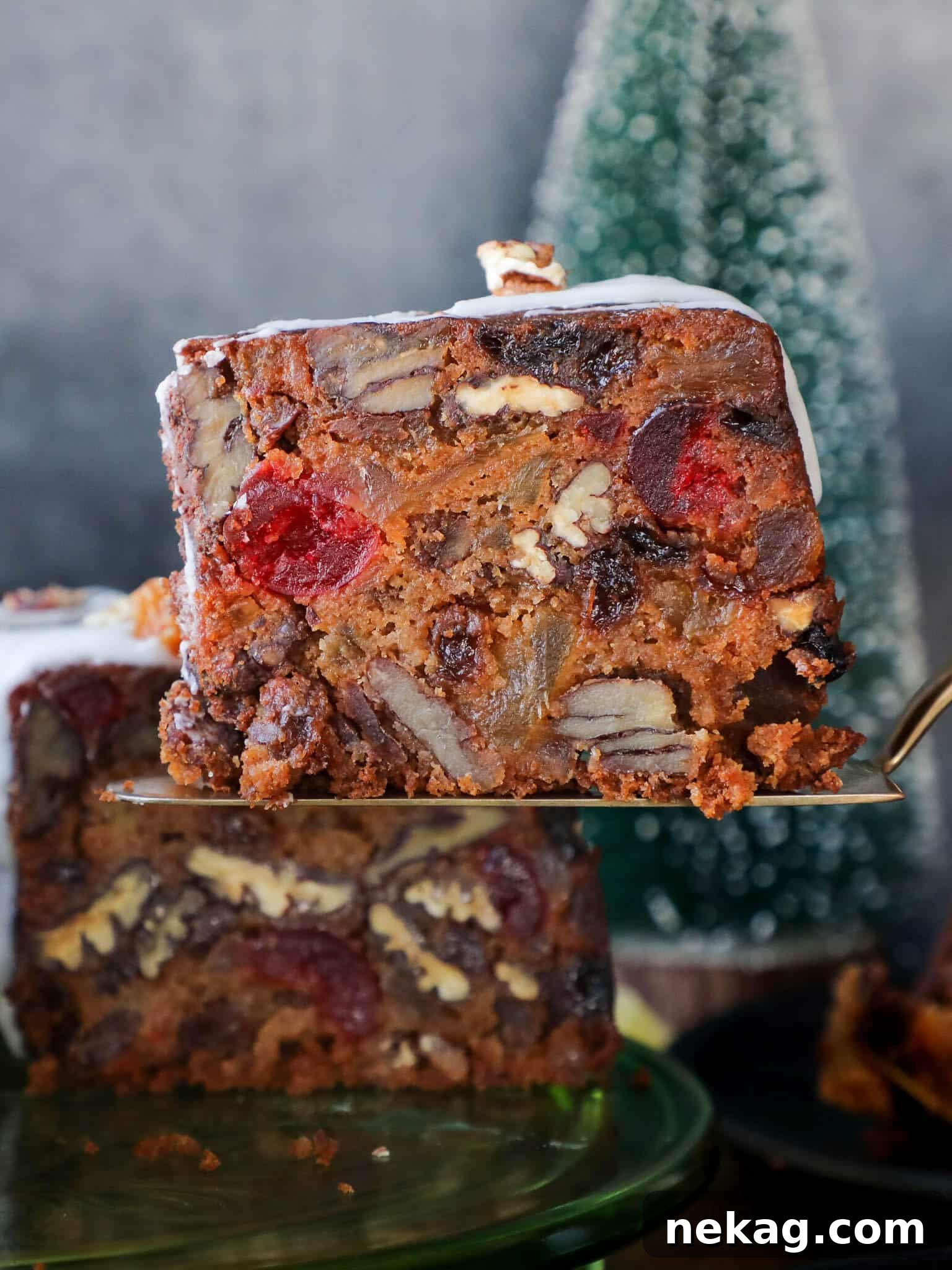 Slice of moist, flavorful Fruit Cake on a cake server, showcasing its rich interior filled with dried fruit and nuts, perfect for festive occasions.