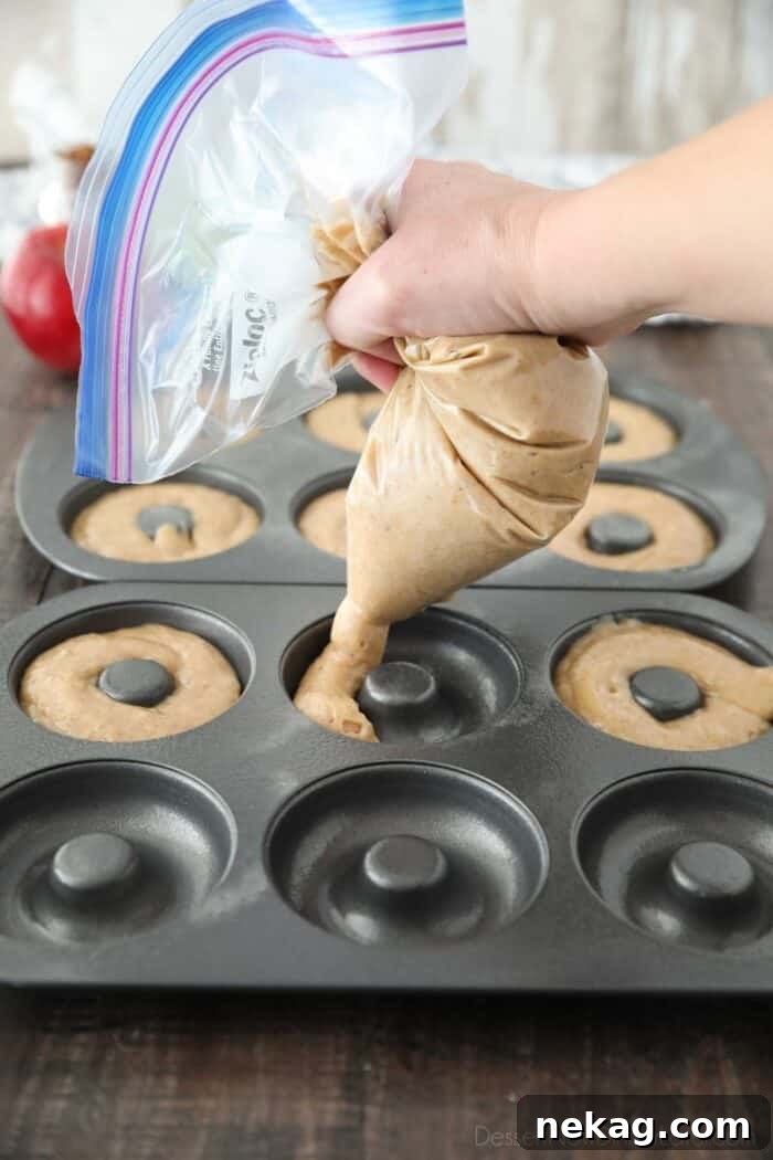 Piping apple cider cake batter into donut pans.
