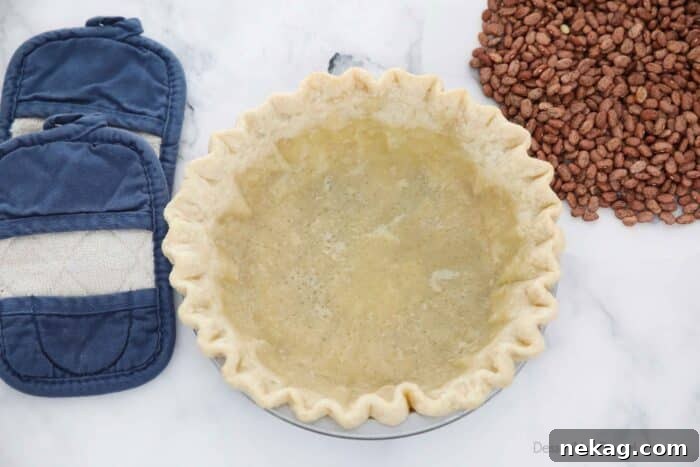 Perfecting Your Blind Baked Pie Crust 9 A partially baked pie crust, golden at the edges, in its pan, after the parchment paper and dry bean weights have been carefully removed.
