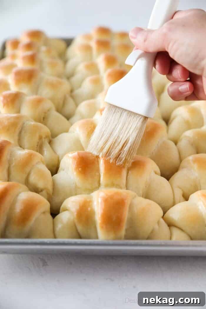 Perfect Homemade Crescent Rolls Video Recipe 13 A hand gently brushes melted butter over the tops of freshly baked, warm crescent rolls, creating a beautiful sheen and adding rich flavor.