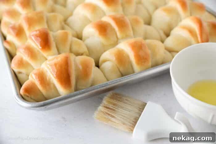 Perfect Homemade Crescent Rolls Video Recipe 4 A close-up view of freshly baked crescent dinner rolls, glistening with melted butter on top, showcasing their golden-brown crust.