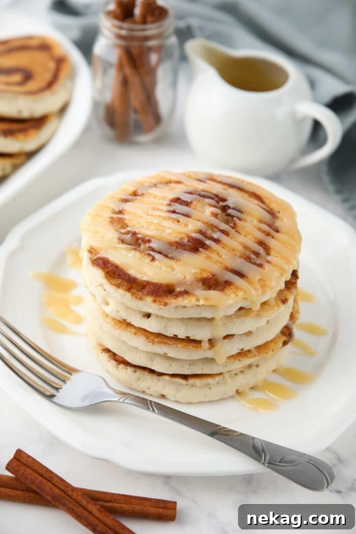 Swirled Cinnamon Pancake Stacks 2 Stack of cinnamon roll pancakes with cream cheese glaze drizzled on top.
