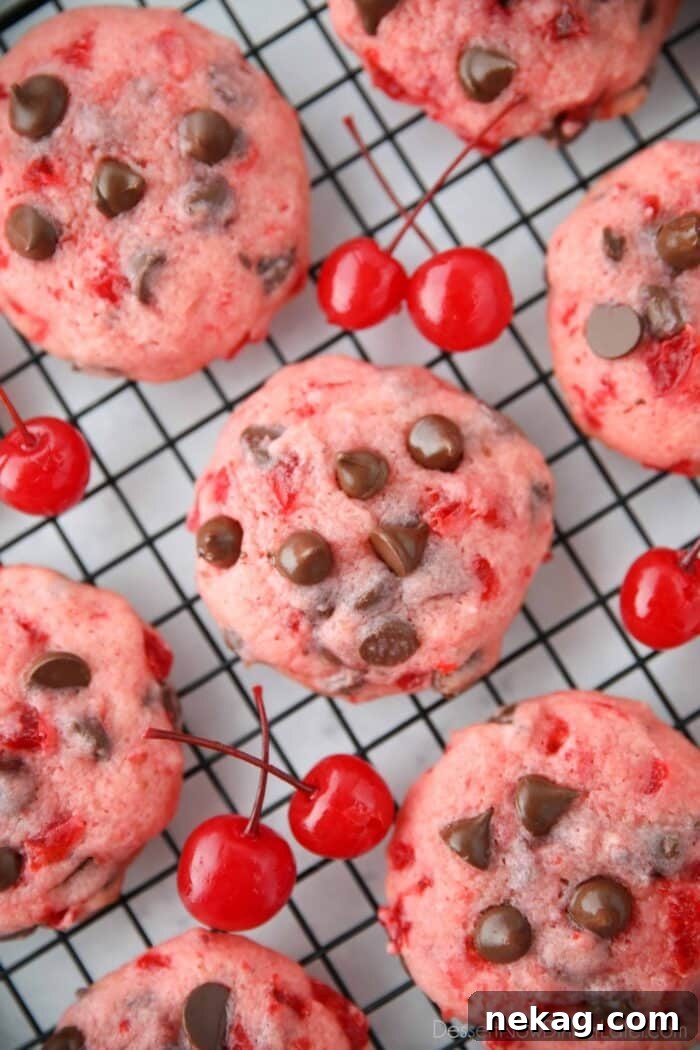Close up top view of cherry chocolate chip cookies on a wire cooling rack with maraschino cherries on the side.