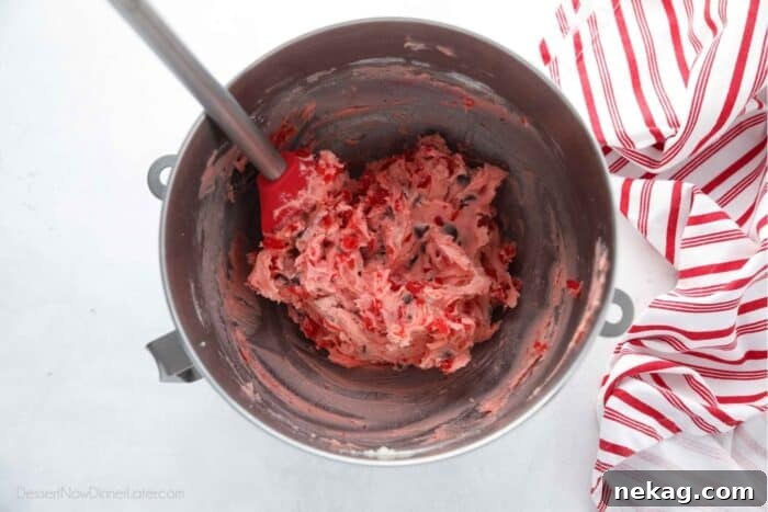 Pink cherry chocolate chip cookie dough in mixing bowl with spatula.