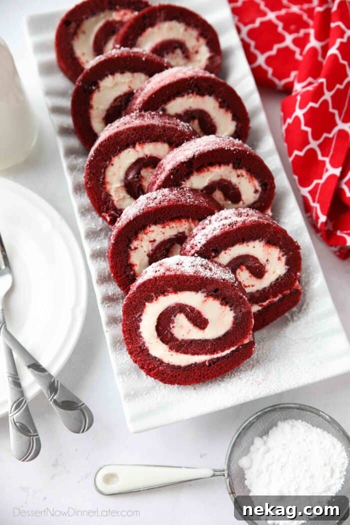 Mastering the Red Velvet Cake Roll 2 Rectangular platter with swirls of red velvet cake roll filled with cream cheese frosting, garnished with powdered sugar.