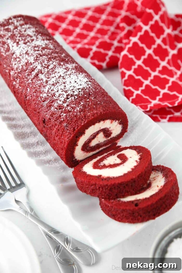 Mastering the Red Velvet Cake Roll 3 Red Velvet Cake Roll on a serving platter with a few slices cut, showing the beautiful spiral.