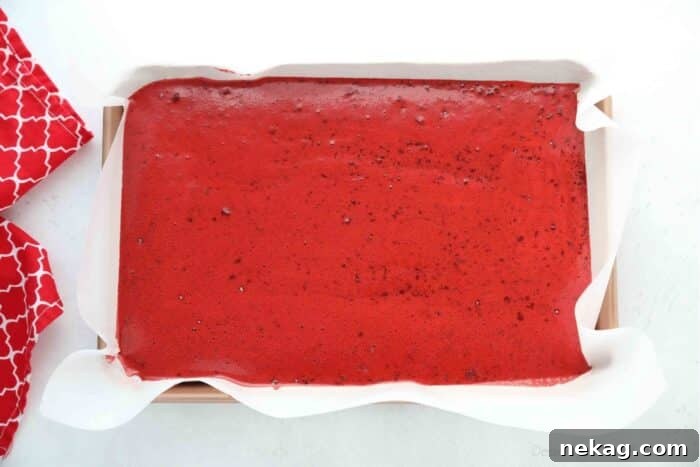 Mastering the Red Velvet Cake Roll 9 Red velvet cake batter spread evenly into a parchment-lined jelly roll pan, ready for baking.