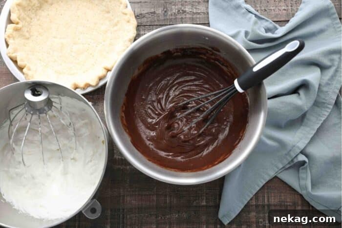 Decadent Chocolate Cream Pie 8 A meticulously arranged composition featuring a freshly baked pie crust in a pan, a bowl of airy sweetened whipped cream, and a bowl of rich chocolate pudding with a whisk, ready for assembly.