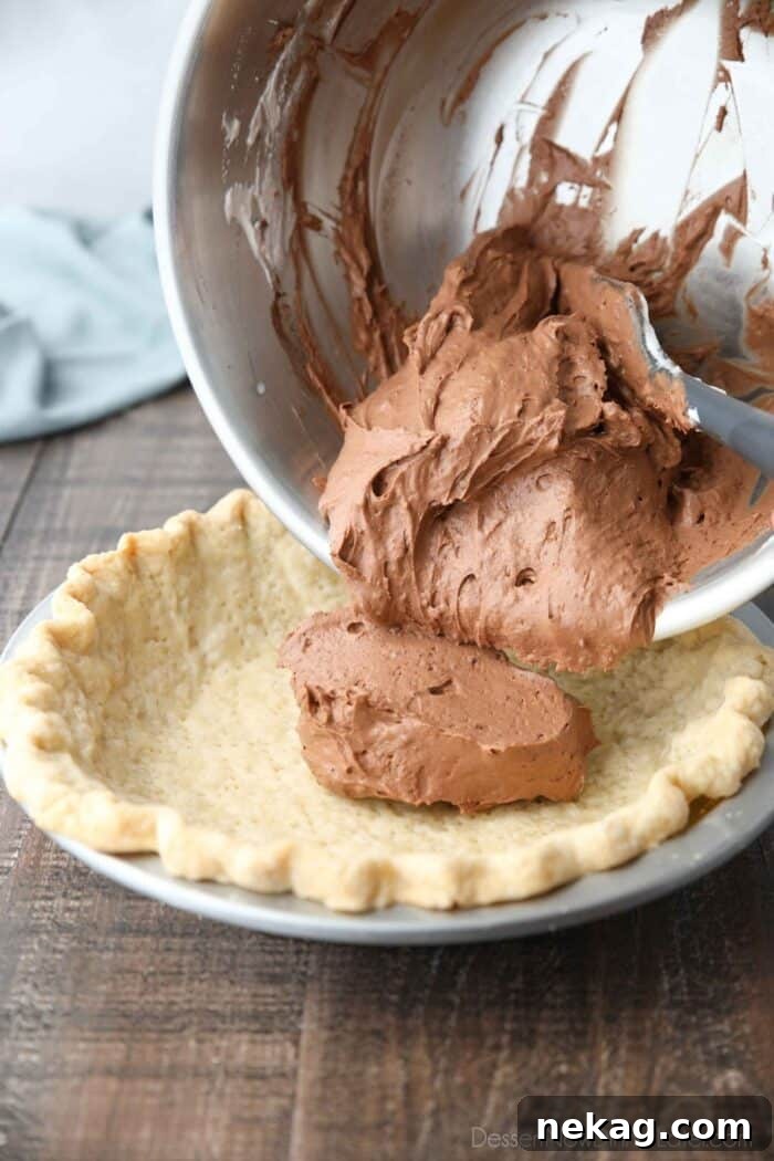 Decadent Chocolate Cream Pie 9 A generous amount of chocolate pudding gently folded with whipped cream being carefully transferred into a golden, pre-baked pie crust, showcasing the creamy texture of the filling.