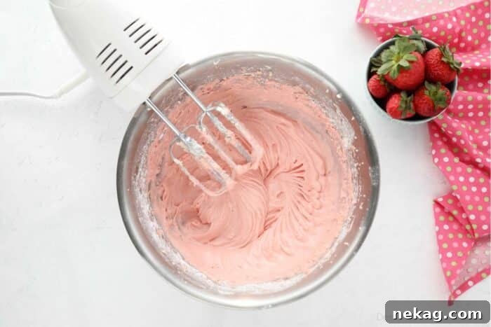 A close-up view of the finished strawberry cream cheese frosting in a mixing bowl, showcasing its smooth, luscious texture, with electric beaters resting nearby.