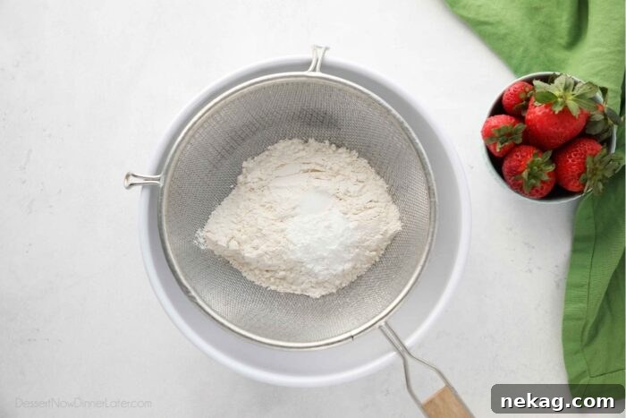 Sifting dry ingredients into a bowl with a fine mesh sieve.