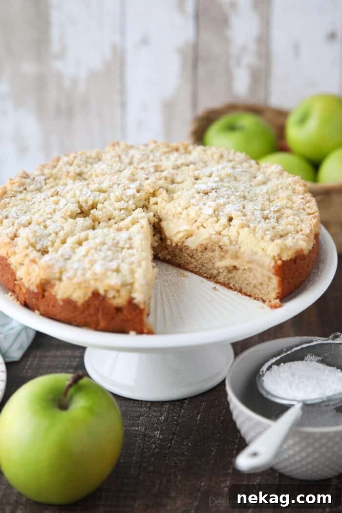 Emerald Isle Apple Cake 3 A beautifully baked Irish Apple Cake presented on a rustic cake stand, with one slice removed revealing the layered interior of cake and apples.