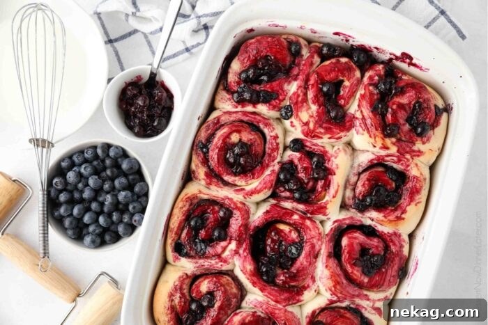 Gooey Blueberry Cinnamon Swirls 12 A close-up view of a baking dish filled with golden-brown blueberry cinnamon rolls, generously brushed with vibrant blueberry sauce, ready for the final lemon glaze.