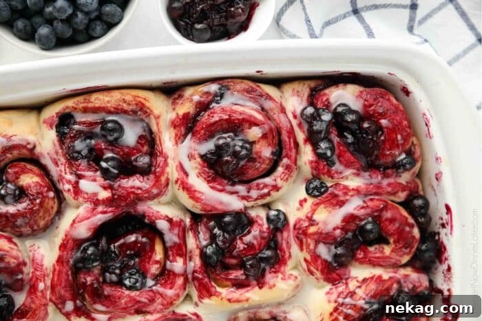 Gooey Blueberry Cinnamon Swirls 5 A close-up view of freshly baked blueberry cinnamon rolls, showing their soft, spiraled interior, generously coated with glistening blueberry sauce and a delicate lemon glaze.
