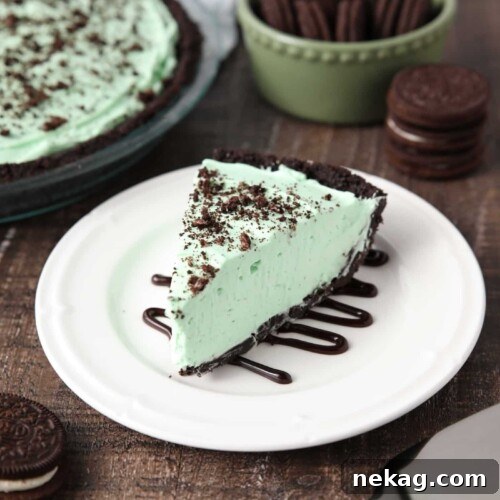 A slice of mint grasshopper pie with an Oreo crust on top of a plate drizzled with chocolate sauce.