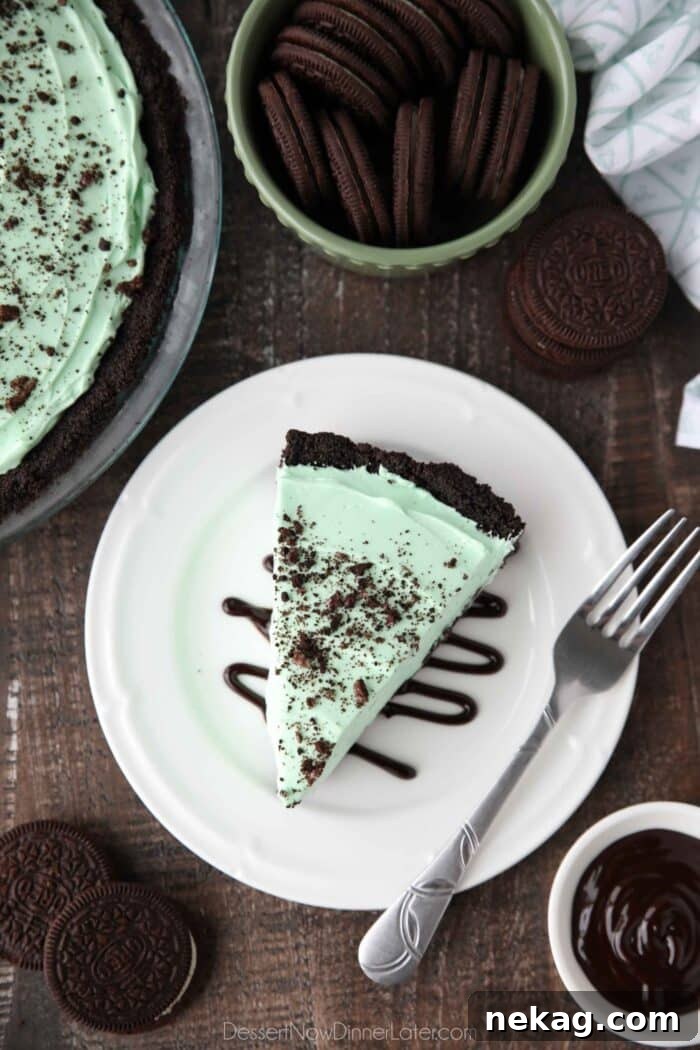 A close-up side view of a slice of no-bake grasshopper pie on a white plate, drizzled with chocolate sauce.