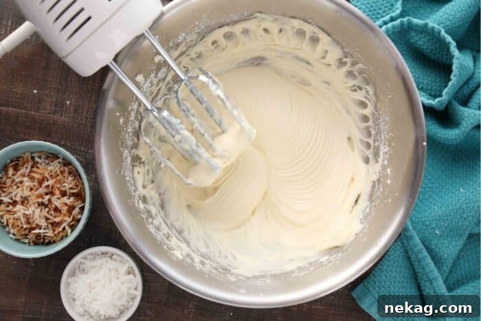A top-down view of a silver mixing bowl with beaters resting inside, filled with perfectly mixed coconut cream cheese frosting, smooth and ready to use.