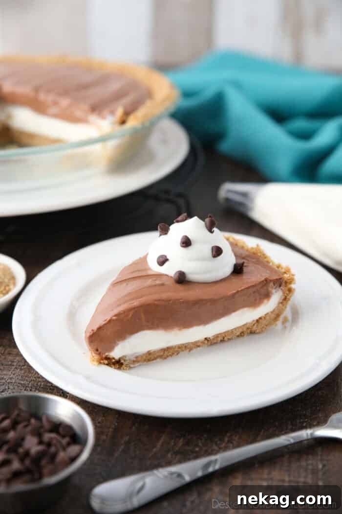 Slice of no-bake chocolate cream cheese pie on a plate, showcasing its golden graham cracker crust, distinct vanilla and chocolate cheesecake layers, and a delicate topping of whipped cream and mini chocolate chips.