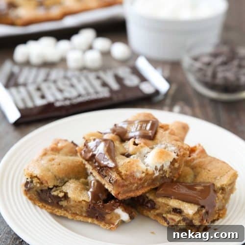 S'mores Cookie Bars are layered with graham crackers, cookie dough with marshmallows, and topped with chocolate bar pieces. It's an ooey gooey melty chocolate s'mores treat!