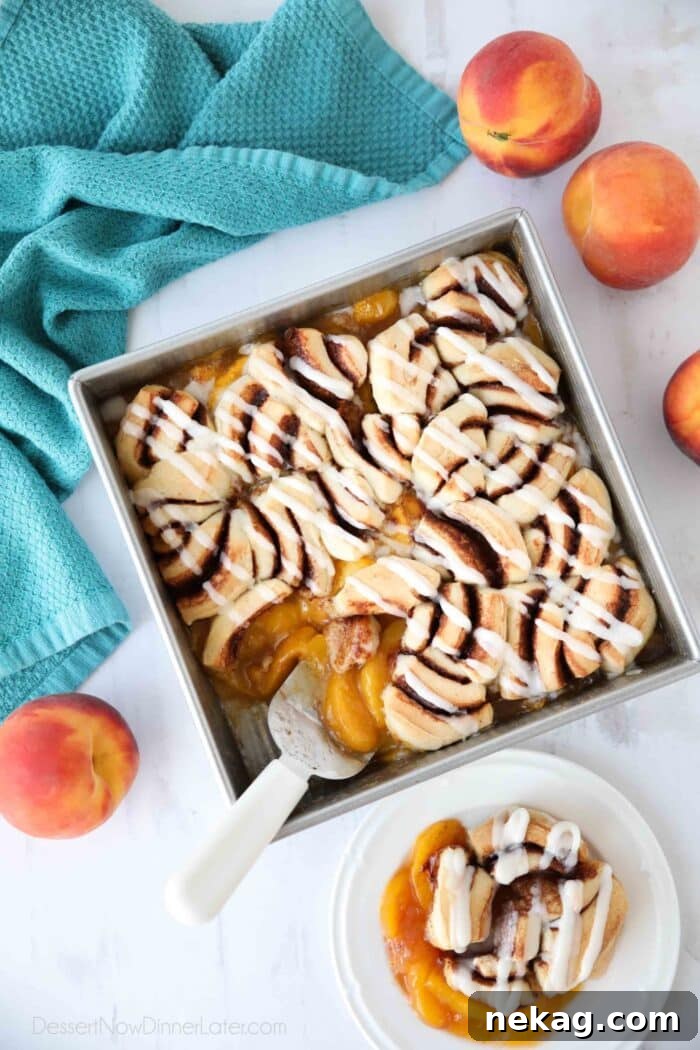 An overhead shot of Cinnamon Roll Peach Cobbler, freshly baked and drizzled with cream cheese frosting, in a baking dish.