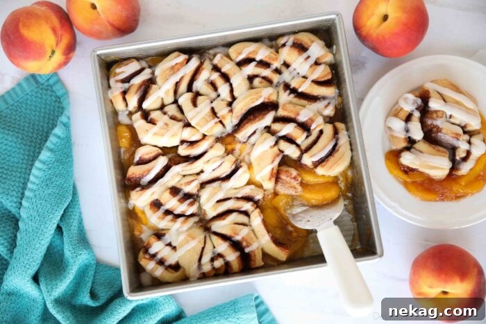 An overhead shot of Cinnamon Roll Peach Cobbler in a baking dish, with golden-brown cinnamon rolls and bubbling peach filling, ready for frosting.