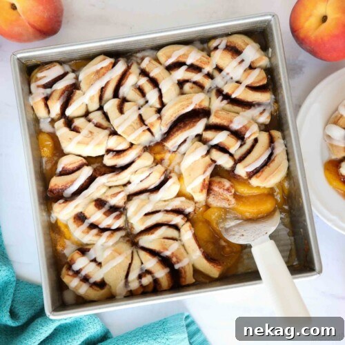 Top view of fresh peach cobbler topped with cinnamon rolls and cream cheese frosting.