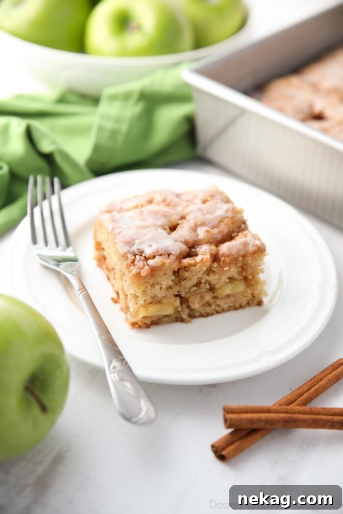 Cinnamon Apple Fritter Cake 2 A square piece of golden-brown glazed apple fritter cake, showcasing its moist texture and apple chunks, resting on a white plate.