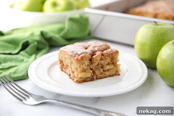 Cinnamon Apple Fritter Cake 11 A single square slice of glazed apple fritter cake, perfectly baked and ready to eat, presented on a white plate.