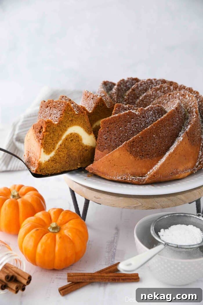 Spiced Pumpkin Bundt with Cream Cheese Swirl 2 A perfectly sliced piece of pumpkin bundt cake with a visible cream cheese swirl, presented on a white plate, ready to be served with a spatula.