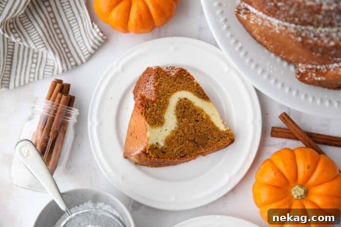 Spiced Pumpkin Bundt with Cream Cheese Swirl 10 A delectable slice of pumpkin cake, beautifully swirled with a creamy cream cheese filling, elegantly presented on a plate.