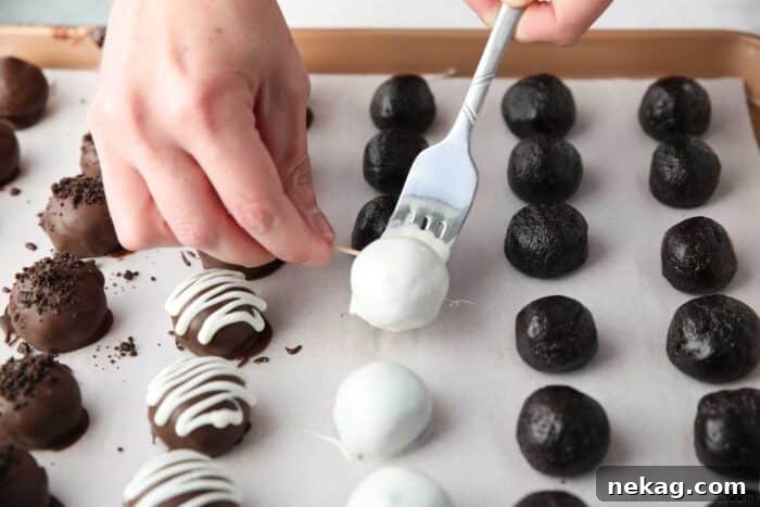 No Bake Oreo Truffles 9 A toothpick is used to carefully push a freshly chocolate-dipped Oreo Ball from a fork onto parchment paper, demonstrating the finishing step of coating.
