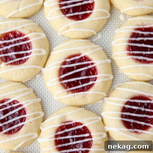 Icing drizzled on top of raspberry thumbprint cookies on a silicone baking mat.