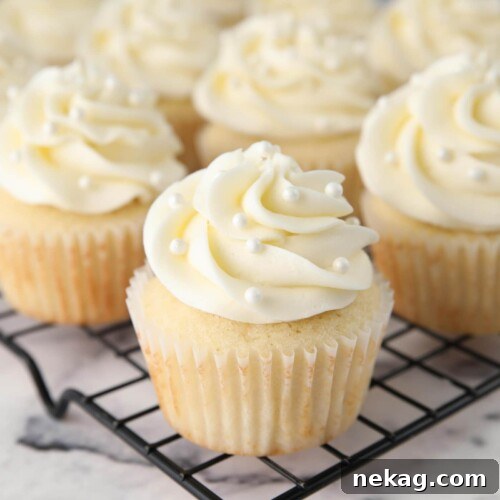 White Cupcakes with vanilla frosting and white sugar pearls on top.