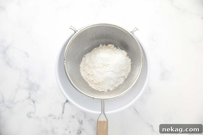Perfectly Fluffy White Cupcakes 5 Dry ingredients, including flour, cornstarch, baking powder, and salt, being sifted into a bowl for a smooth cupcake batter.