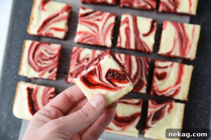A hand holding a single red velvet cream cheese brownie, showcasing its perfect swirled top and fudgy texture.