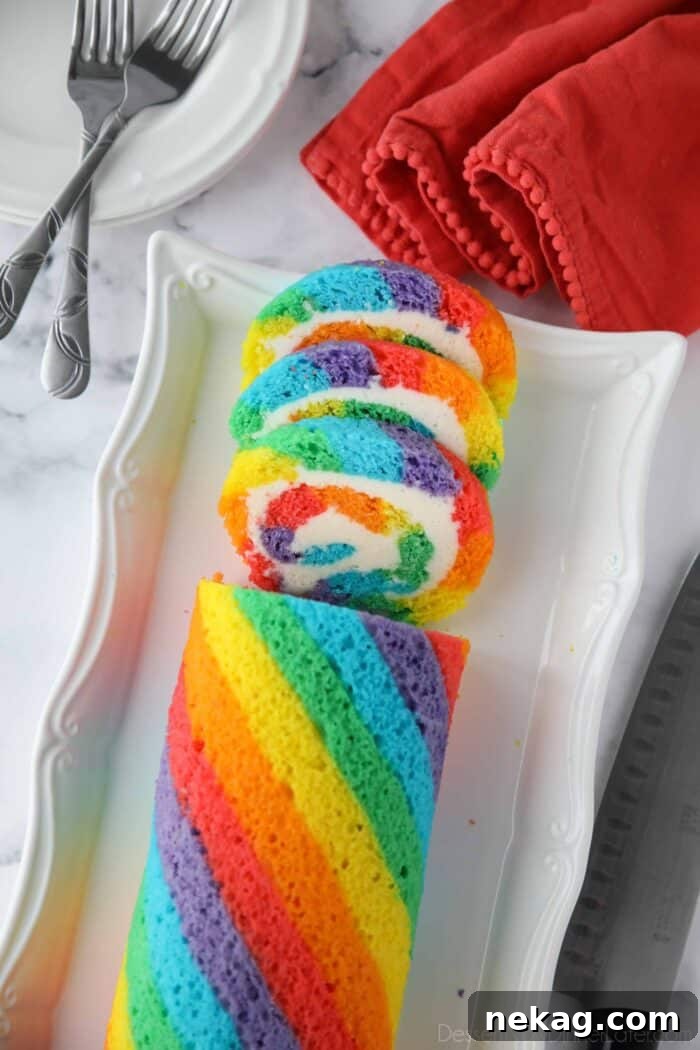 Rainbow cake roll on a platter with a few slices cut.