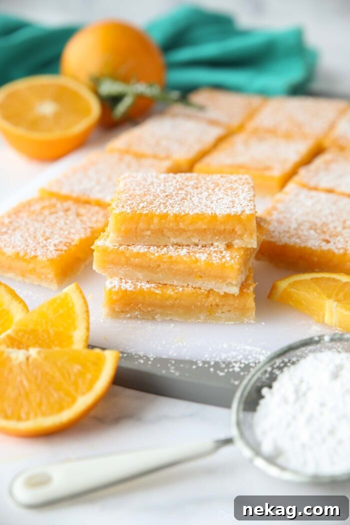 Golden Citrus Bars 2 A stack of golden orange bars, generously dusted with powdered sugar, showcasing their vibrant color and delicate texture.